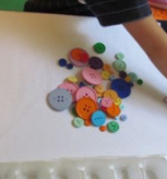 Student reaching over a tray of buttons of variable sizes and colors.